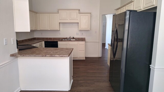 kitchen featuring dark wood-type flooring, black dishwasher, a peninsula, freestanding refrigerator, and a sink