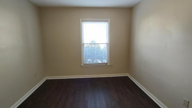 spare room with baseboards and dark wood-style floors