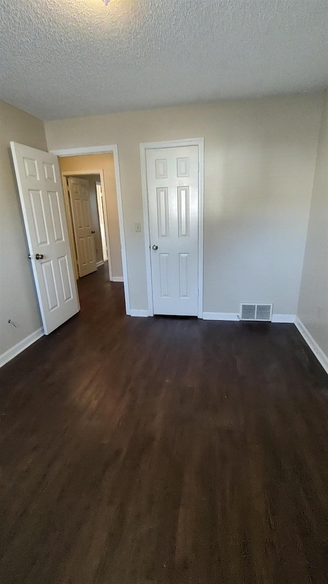 unfurnished bedroom with visible vents, a textured ceiling, baseboards, and dark wood-style flooring