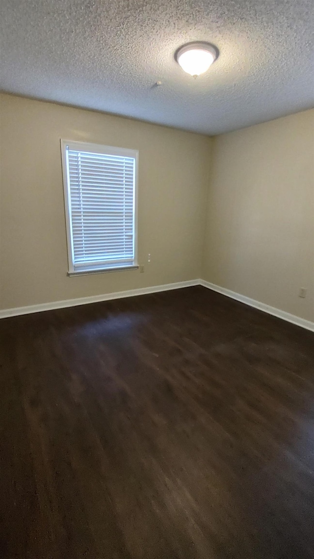 empty room featuring dark wood-type flooring, baseboards, and a textured ceiling