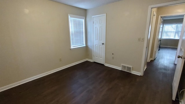 unfurnished bedroom with dark wood finished floors, visible vents, baseboards, and a closet