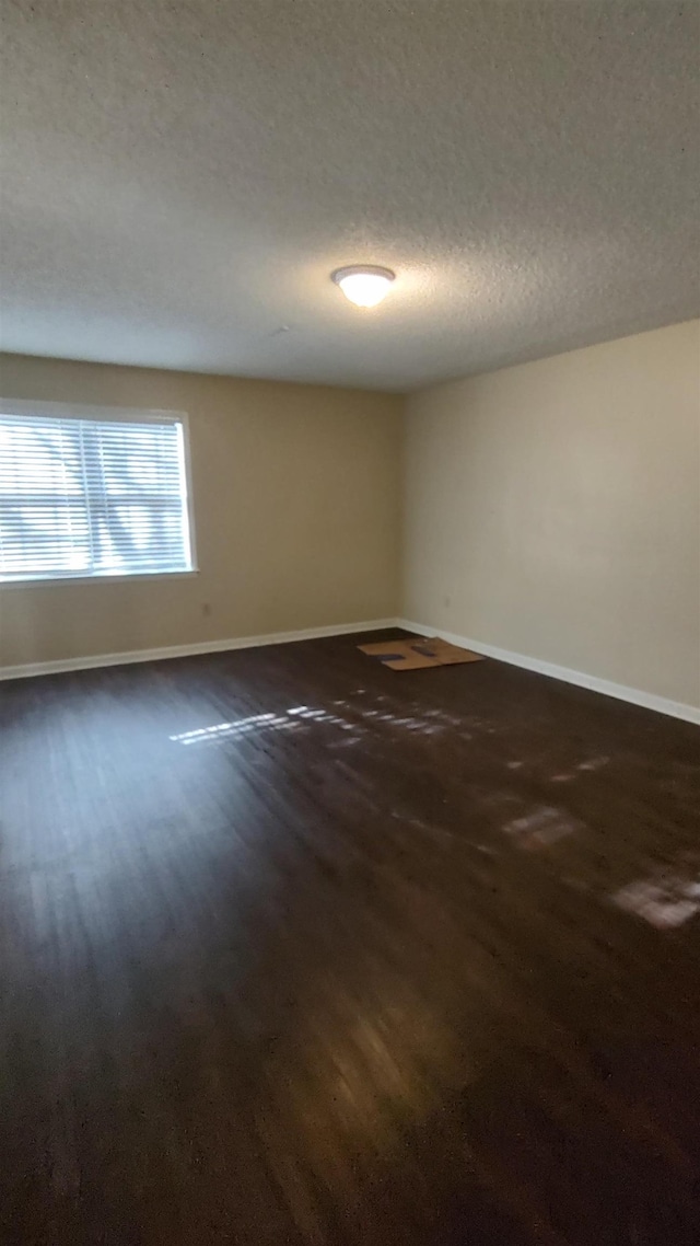 empty room featuring a textured ceiling, baseboards, and dark wood-style flooring