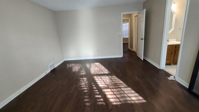 unfurnished bedroom with wood finished floors, visible vents, ensuite bathroom, and baseboards