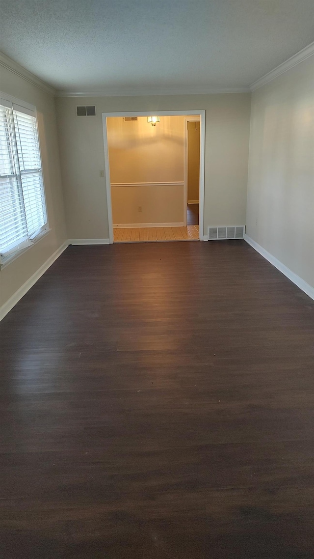 empty room featuring dark wood-style floors, visible vents, and ornamental molding