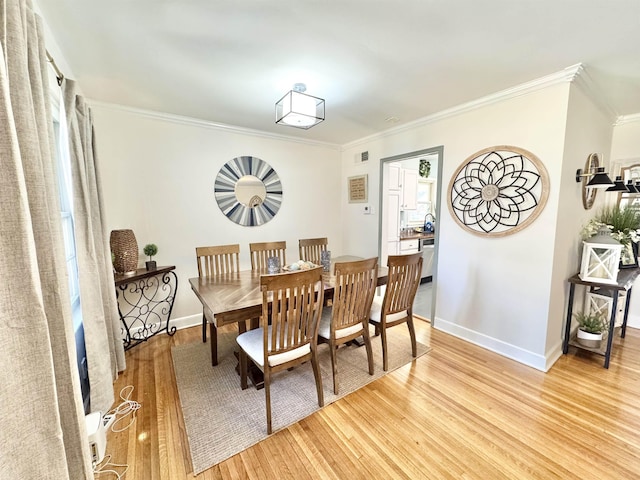 dining room featuring light wood-type flooring, baseboards, and ornamental molding