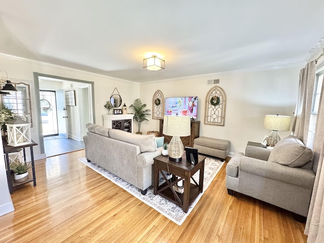 living area with visible vents, a healthy amount of sunlight, light wood-style flooring, and crown molding