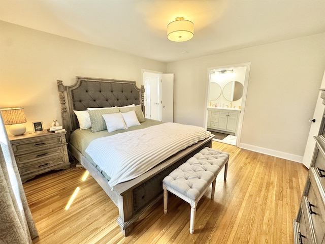 bedroom with connected bathroom, baseboards, and light wood-style flooring