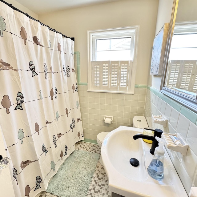 bathroom featuring a sink, toilet, tile walls, and wainscoting