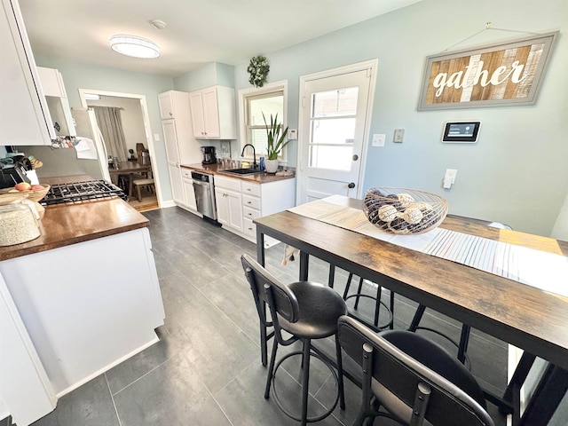 kitchen with dark countertops, gas range, dishwasher, white cabinetry, and a sink