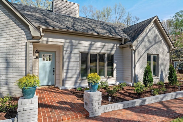 entrance to property featuring brick siding and a shingled roof