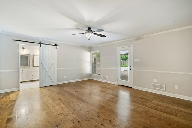 interior space with a barn door, visible vents, wood-type flooring, and ornamental molding