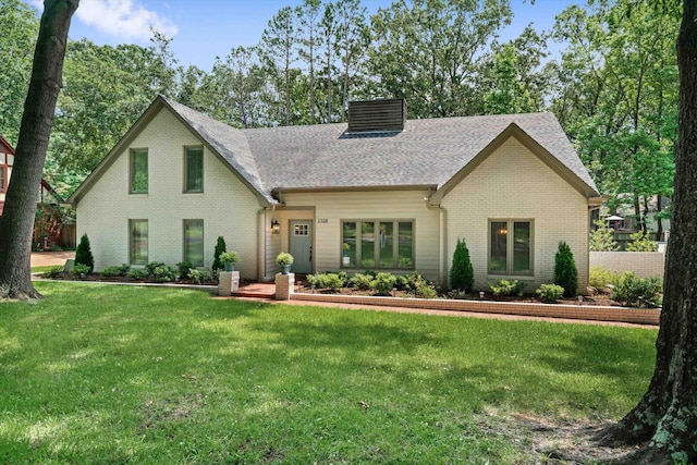 view of front of property featuring a front yard, a chimney, brick siding, and a shingled roof