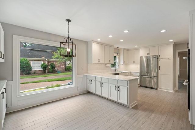 kitchen with a peninsula, light wood-style flooring, white cabinets, high end refrigerator, and tasteful backsplash