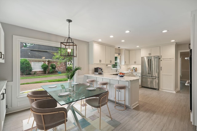 kitchen featuring light wood finished floors, high end fridge, a peninsula, and backsplash