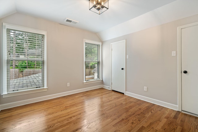 empty room featuring visible vents, baseboards, lofted ceiling, light wood-style floors, and a notable chandelier