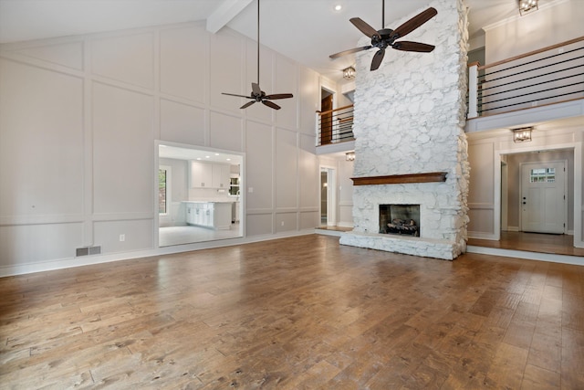 unfurnished living room with visible vents, beam ceiling, wood-type flooring, a stone fireplace, and a decorative wall