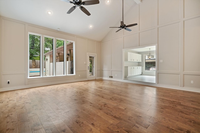 unfurnished living room with ceiling fan with notable chandelier, high vaulted ceiling, wood finished floors, and a decorative wall