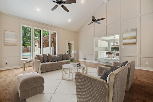 living area featuring a decorative wall, ceiling fan with notable chandelier, high vaulted ceiling, and light wood-type flooring