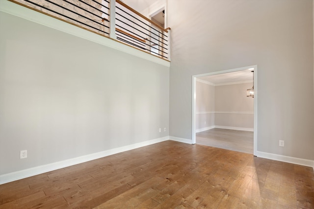 empty room with a notable chandelier, a towering ceiling, baseboards, and wood-type flooring