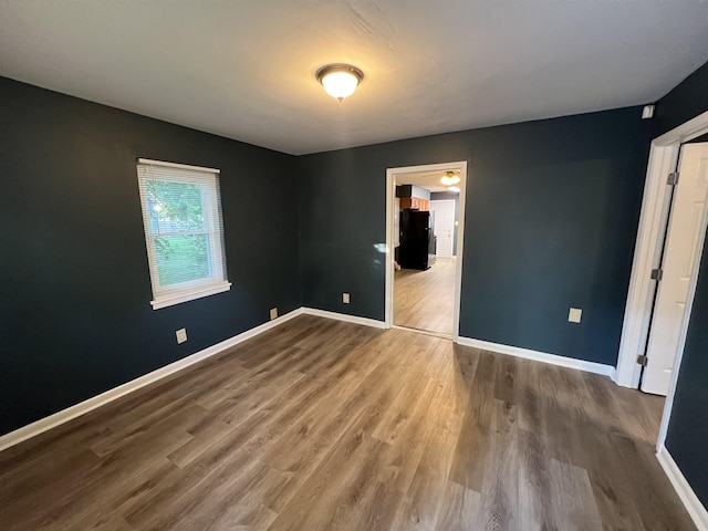 unfurnished bedroom featuring freestanding refrigerator, baseboards, and wood finished floors