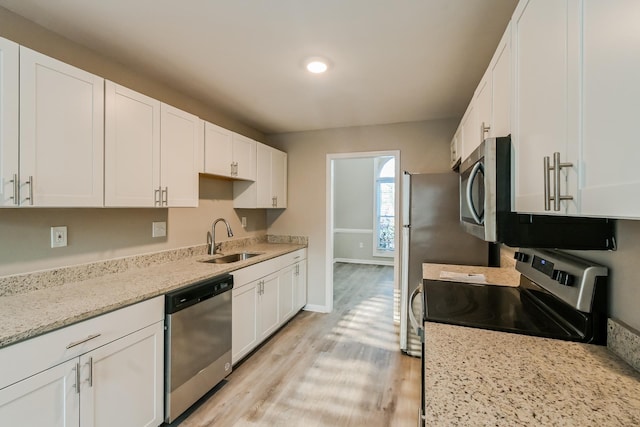 kitchen with light stone counters, light wood-style flooring, appliances with stainless steel finishes, white cabinets, and a sink