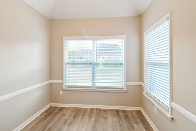 spare room with light wood-type flooring, baseboards, and vaulted ceiling