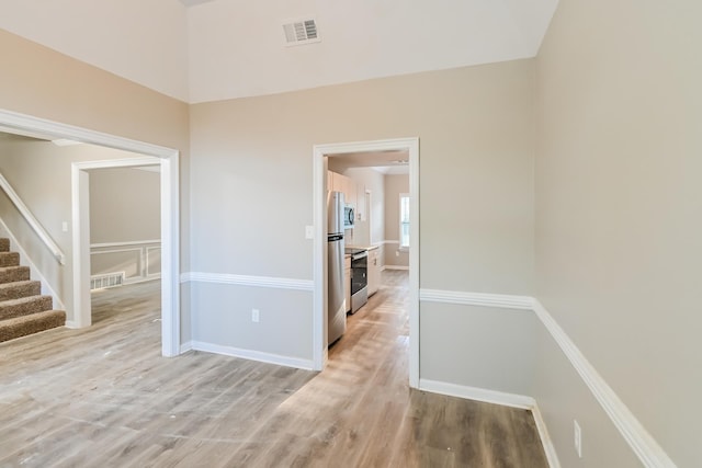 hall featuring visible vents, baseboards, light wood-style flooring, and stairs