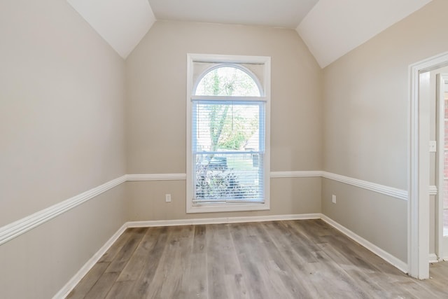 spare room with light wood finished floors, baseboards, and lofted ceiling