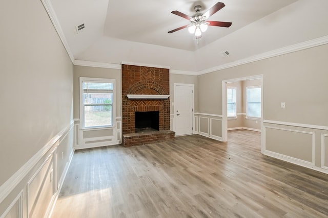 unfurnished living room featuring plenty of natural light, a brick fireplace, a decorative wall, and a tray ceiling