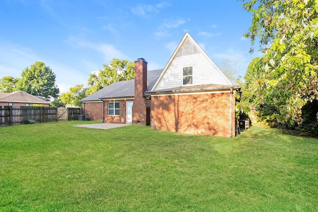 back of property featuring brick siding, a chimney, a yard, and fence