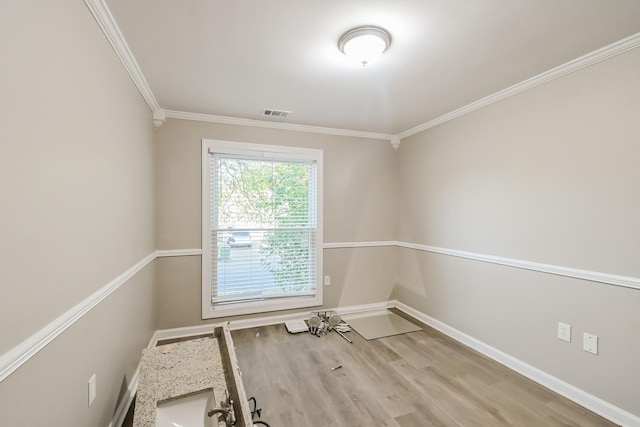 empty room with visible vents, wood finished floors, baseboards, and ornamental molding