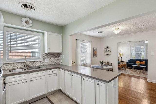 kitchen featuring visible vents, light wood-style flooring, a sink, a peninsula, and white cabinets