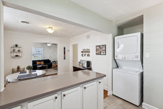 kitchen featuring stacked washer / dryer, a textured ceiling, white cabinetry, and visible vents