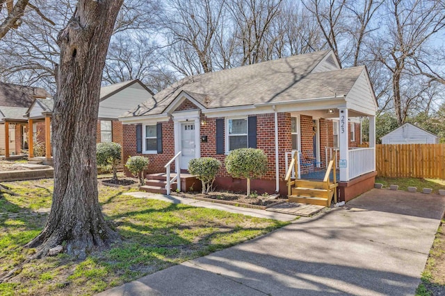 view of front facade featuring brick siding, covered porch, a shingled roof, and fence