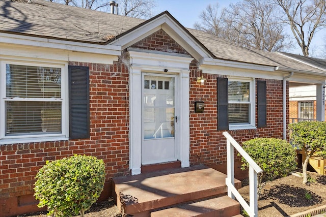 view of exterior entry featuring brick siding and a shingled roof