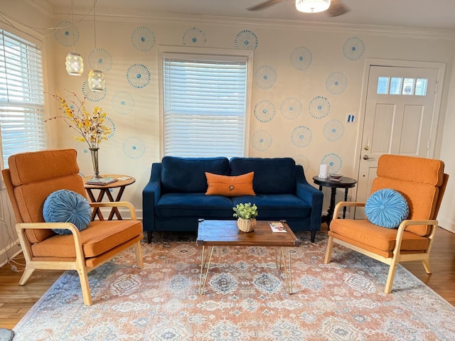 living area featuring ceiling fan, wood finished floors, ornamental molding, and wallpapered walls