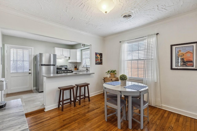 dining space featuring visible vents, light wood-style flooring, baseboards, and ornamental molding