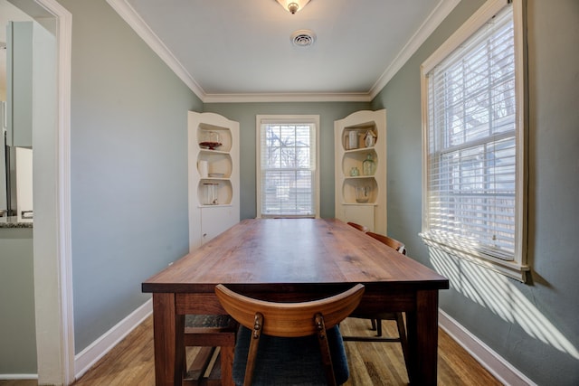 dining space with baseboards, wood finished floors, visible vents, and ornamental molding