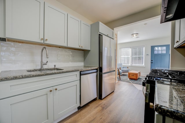 kitchen featuring light wood-style flooring, a sink, backsplash, stainless steel appliances, and light stone countertops