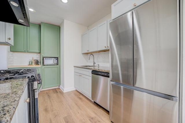 kitchen featuring light wood finished floors, green cabinets, range hood, appliances with stainless steel finishes, and a sink