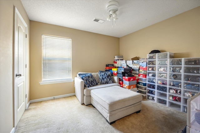 living area featuring visible vents, baseboards, carpet floors, a textured ceiling, and a ceiling fan