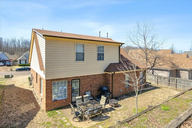 rear view of house featuring brick siding, a patio area, an outdoor fire pit, and fence