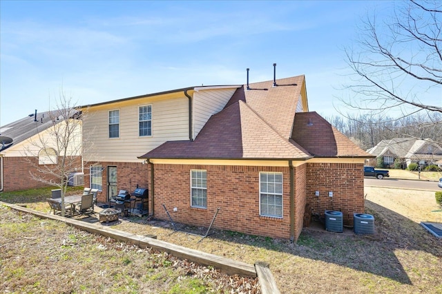 back of property featuring brick siding, central air condition unit, a fire pit, and roof with shingles