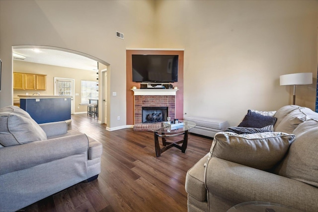 living area with visible vents, baseboards, a fireplace, arched walkways, and dark wood-style flooring