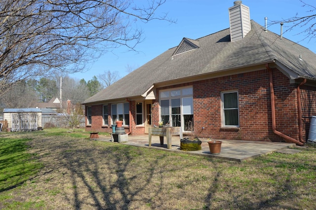 back of house with brick siding, a lawn, a patio, and roof with shingles