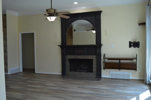 unfurnished living room featuring a tiled fireplace, visible vents, crown molding, and wood finished floors