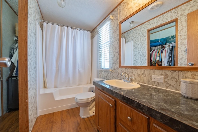 bathroom with toilet, a textured ceiling, wood finished floors, wallpapered walls, and vanity