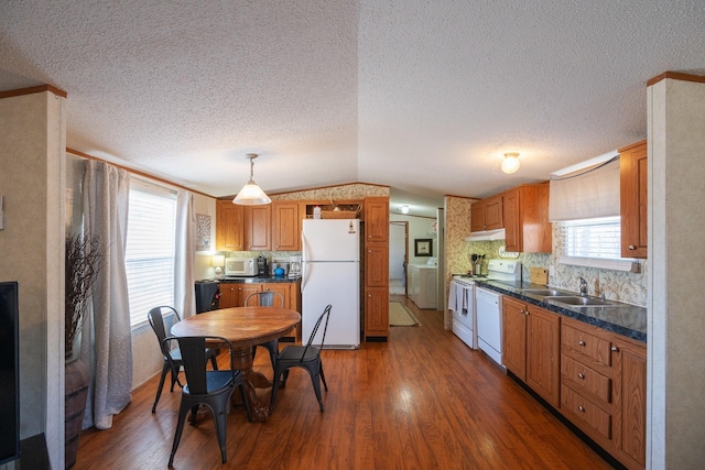 kitchen with washer / dryer, white appliances, wood finished floors, and a sink