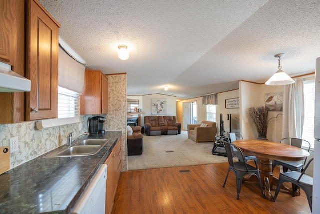 kitchen featuring brown cabinets, a sink, dark countertops, lofted ceiling, and dishwasher