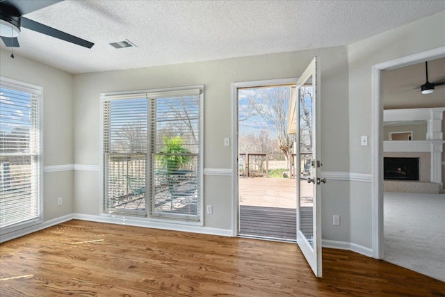 doorway with visible vents, a ceiling fan, a textured ceiling, wood finished floors, and a brick fireplace